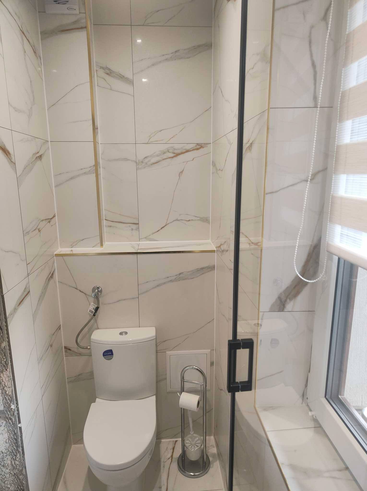 Wykończona łazienka z białymi płytkami imitującymi marmur, złotymi akcentami i kabiną prysznicową z czarnymi detalami, prezentująca nowoczesny design.