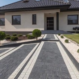 Spark Brukarstwo - Nowoczesny podjazd do domu wyłożony szarą kostką z białymi obrzeżami, z elementami małej architektury i zadbanym trawnikiem.