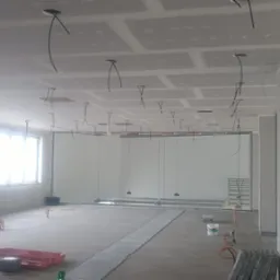 Wnętrze biura w trakcie prac wykończeniowych: zamontowane płyty karton-gips na suficie z wystającymi kablami, przygotowane podłoże pod posadzkę.