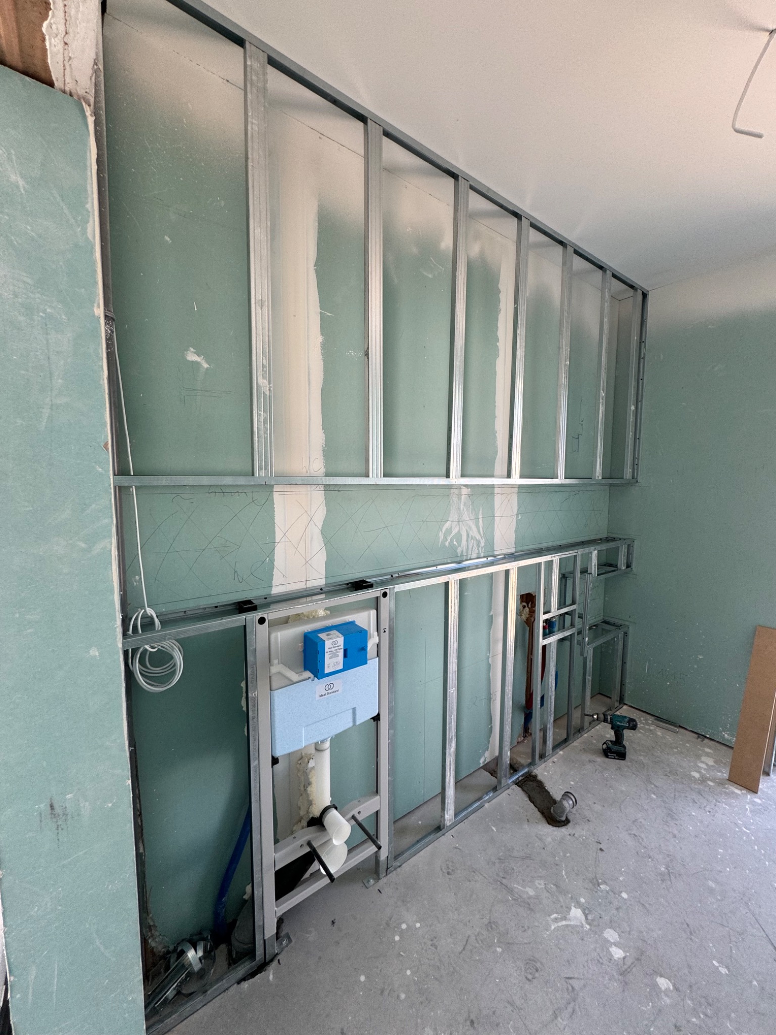 Konstrukcja z profili stalowych pod zabudowę z płyt karton-gips, z widoczną instalacją podtynkową WC i częściowo położonymi płytami, w pomieszczeniu w trakcie remontu.