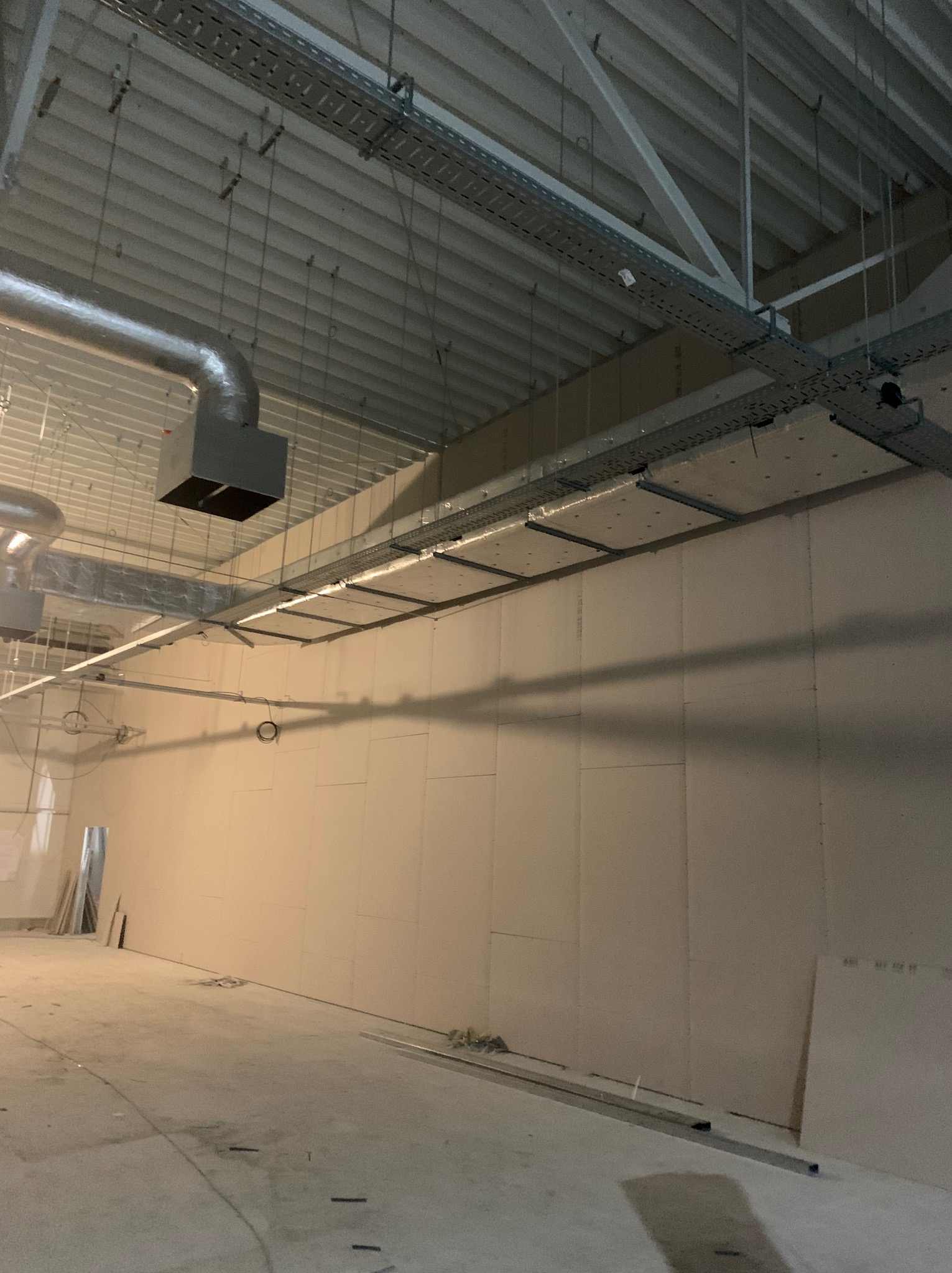 Wnętrze w trakcie prac wykończeniowych, ściany pokryte płytami gipsowo-kartonowymi, widoczne instalacje pod sufitem, surowy beton na podłodze.