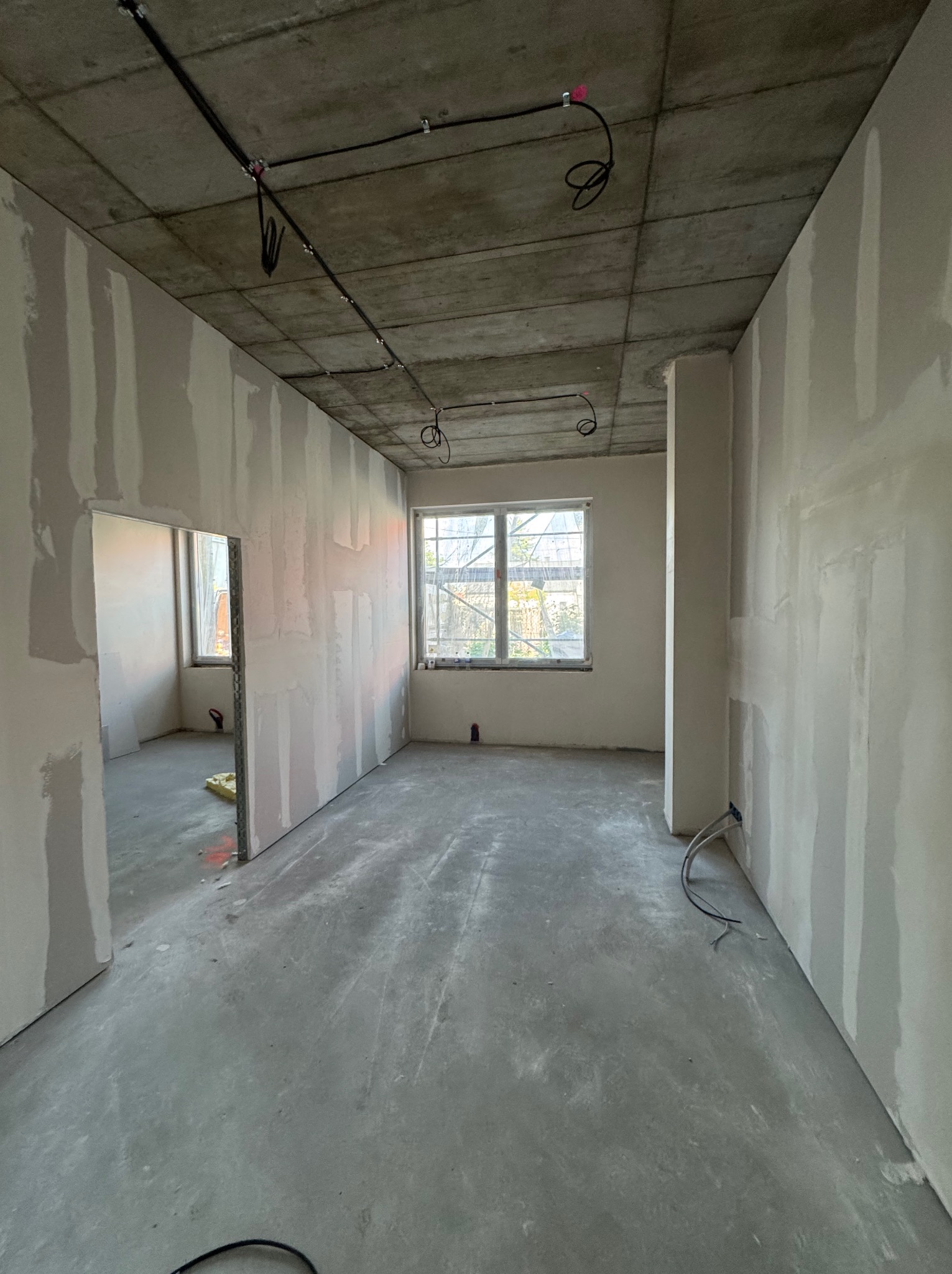 Surowe wnętrze w trakcie prac wykończeniowych: ściany z płytami, widoczne przewody elektryczne na suficie. Stan surowy, przygotowanie do dalszych prac.