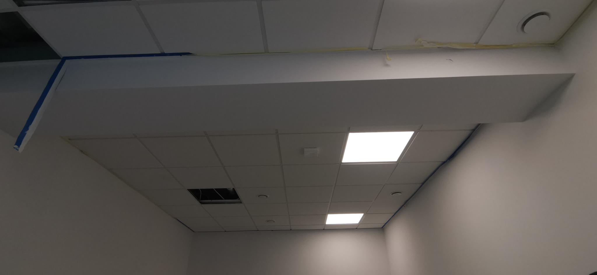 Sufit podwieszany z widocznymi elementami maskującymi i taśmą malarską, fragment instalacji elektrycznej bez oprawy oświetleniowej.