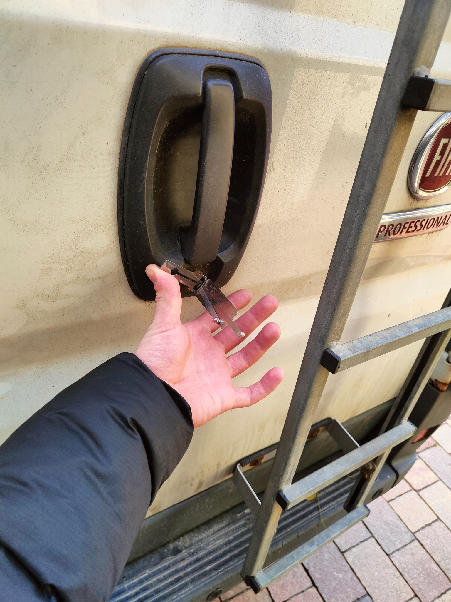 Otwieranie zamka drzwi samochodu za pomocą wytrychu, widoczna drabina na tylnych drzwiach.