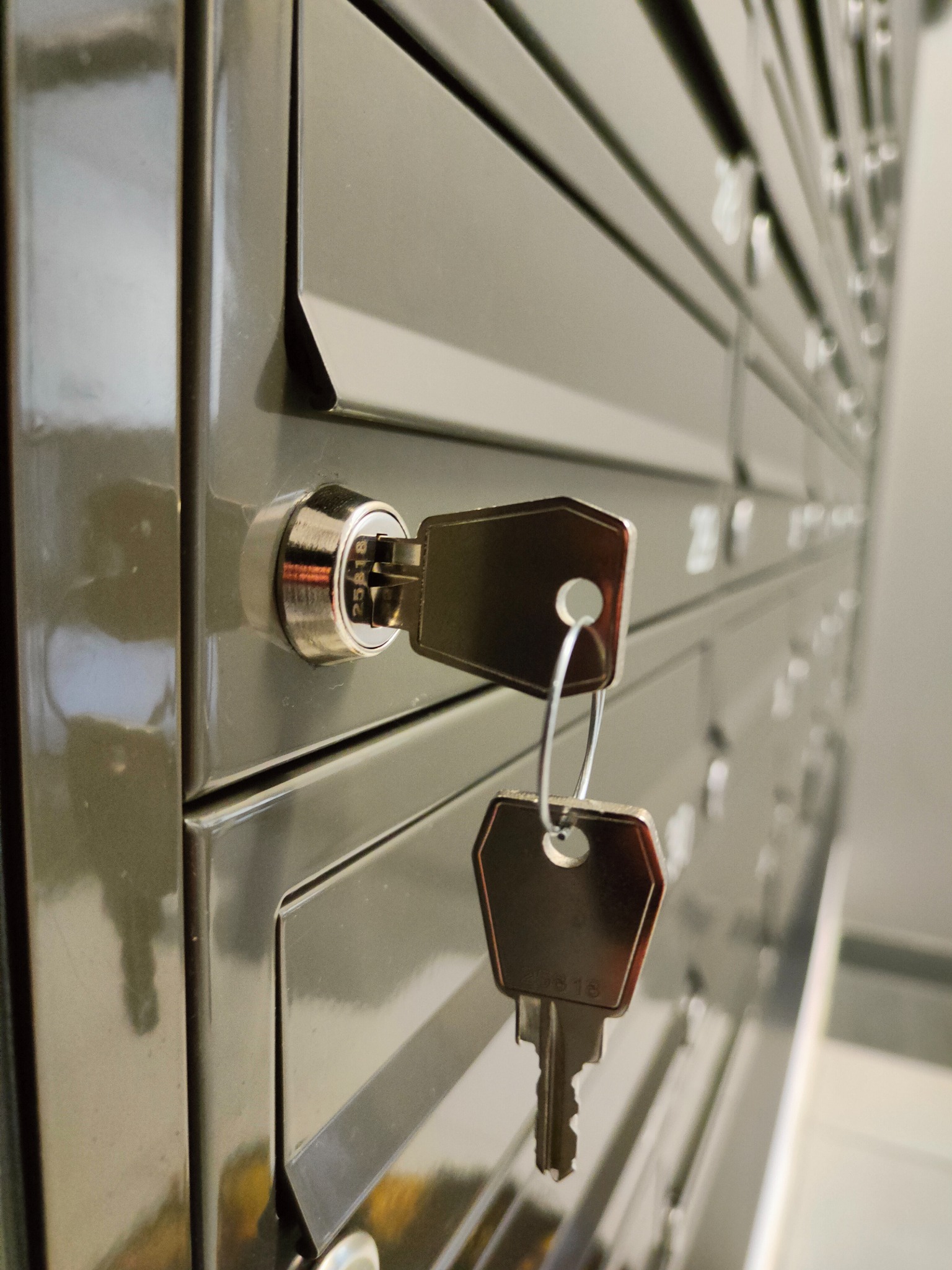 Szereg metalowych skrzynek pocztowych z kluczem w zamku jednej z nich, widoczny numer 25818 na kluczu.