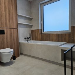 Home Finish Usługi remontowo-budowlane Maciej Twarowski - Nowoczesna łazienka z drewnianymi akcentami: zabudowa, półki, obudowa wanny. Minimalistyczna armatura w czerni, jasne płytki podłogowe i ścienne. Duże okno.