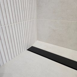 Home Finish Usługi remontowo-budowlane Maciej Twarowski - Nowoczesny odpływ liniowy w kabinie prysznicowej z jasnymi płytkami. Ściana z dekoracyjną fakturą pionowych pasków. Minimalistyczny design.