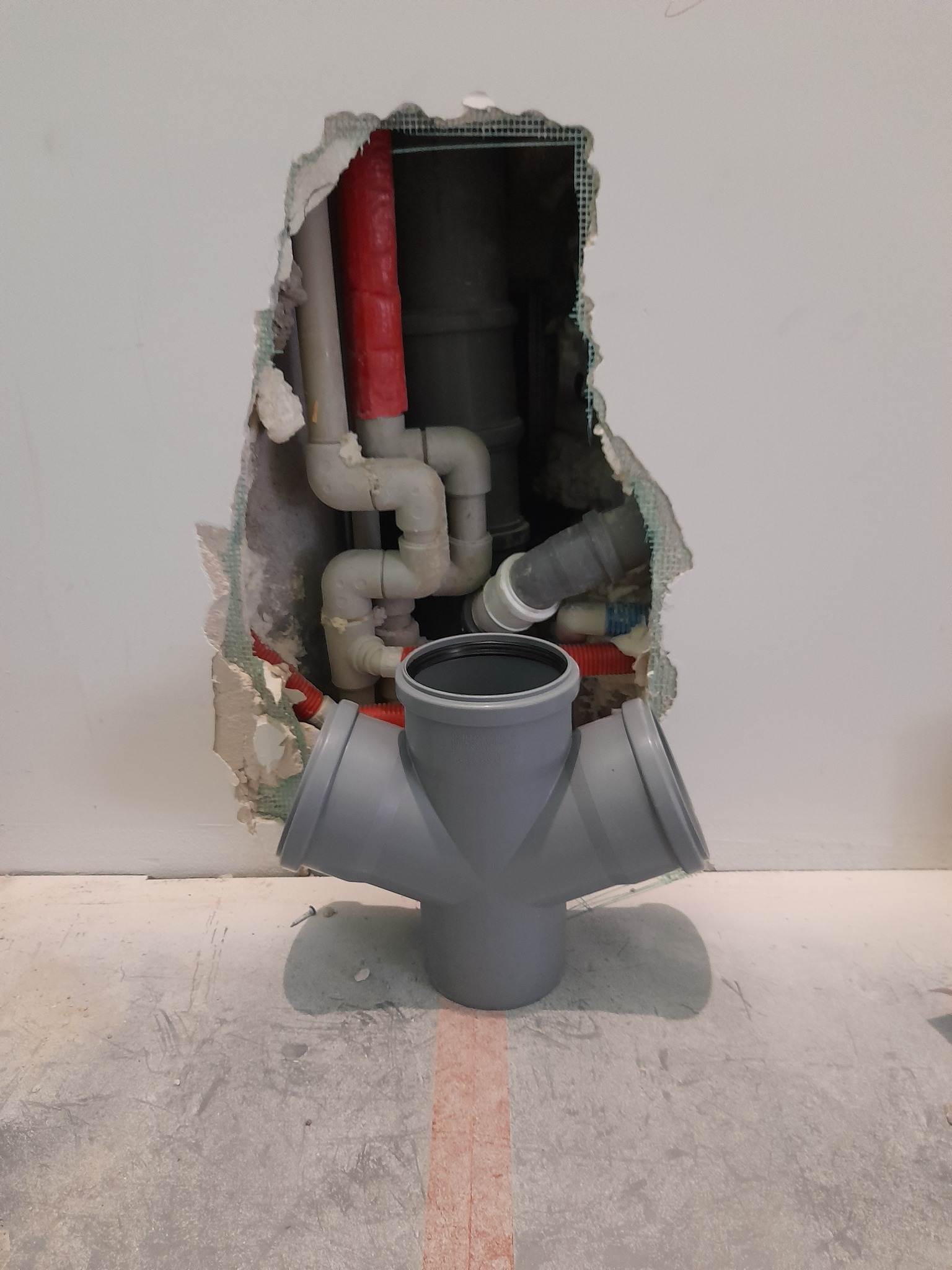 Instalacja kanalizacyjna w trakcie wykonywania w Białymstoku: widoczne rury w ścianie z uszkodzonym tynkiem oraz trójnik kanalizacyjny na podłodze.