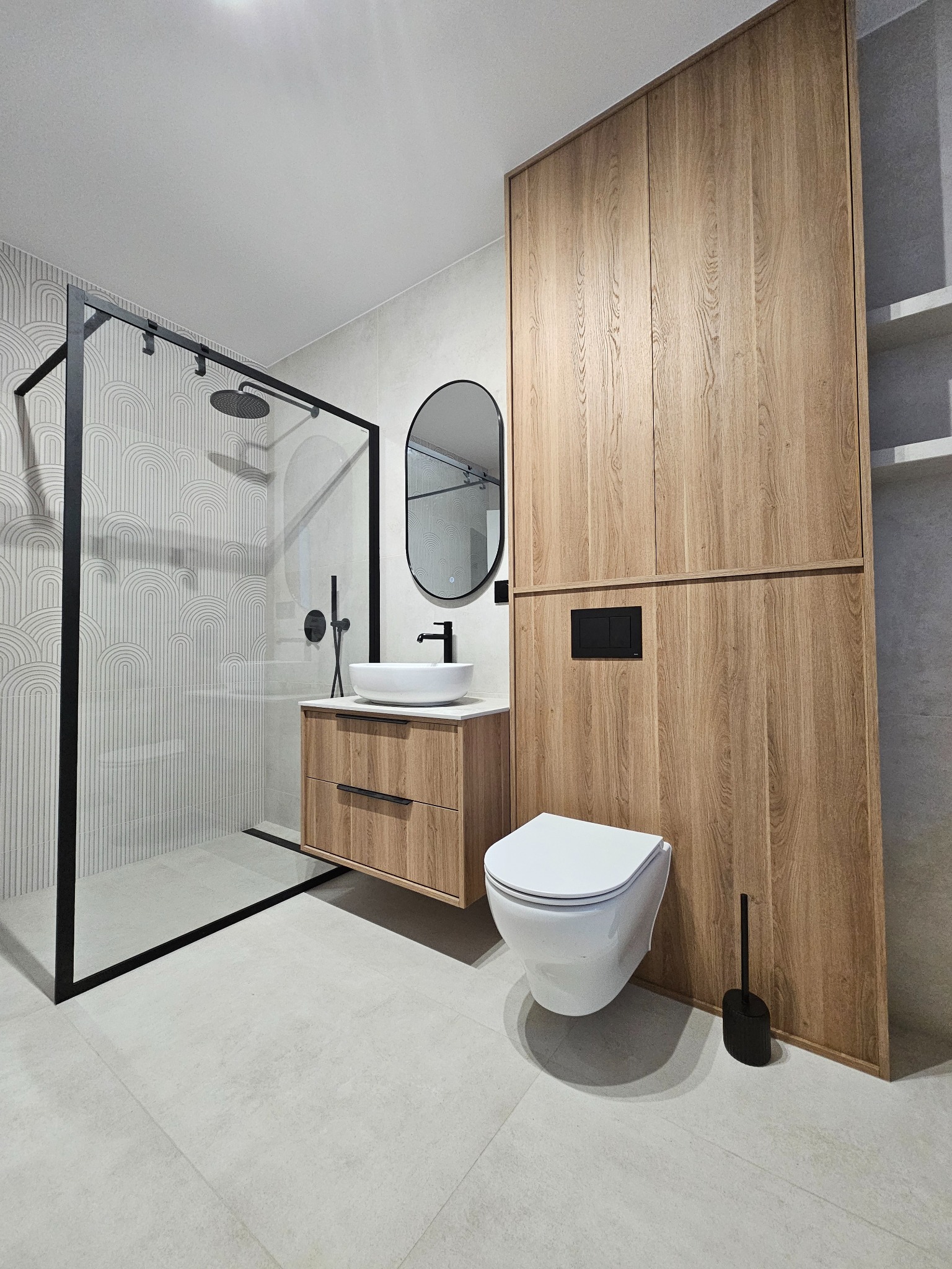 Nowoczesna łazienka z kabiną prysznicową typu walk-in, umywalką nablatową na szafce z drewnianym fornirem i zabudową meblową z toaletą w minimalistycznym stylu.