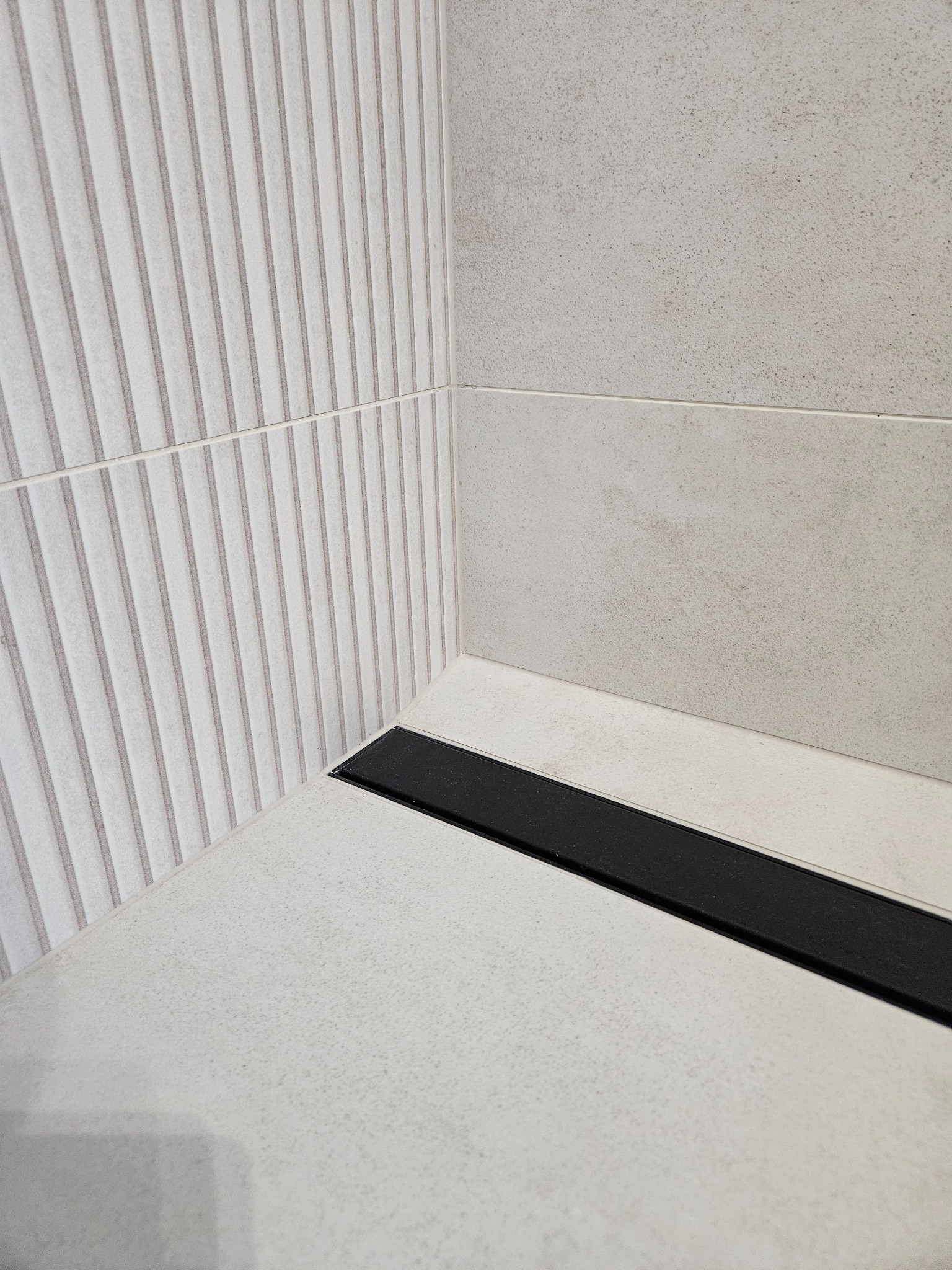 Nowoczesny odpływ liniowy w kabinie prysznicowej z jasnymi płytkami. Ściana z dekoracyjną fakturą pionowych pasków. Minimalistyczny design.