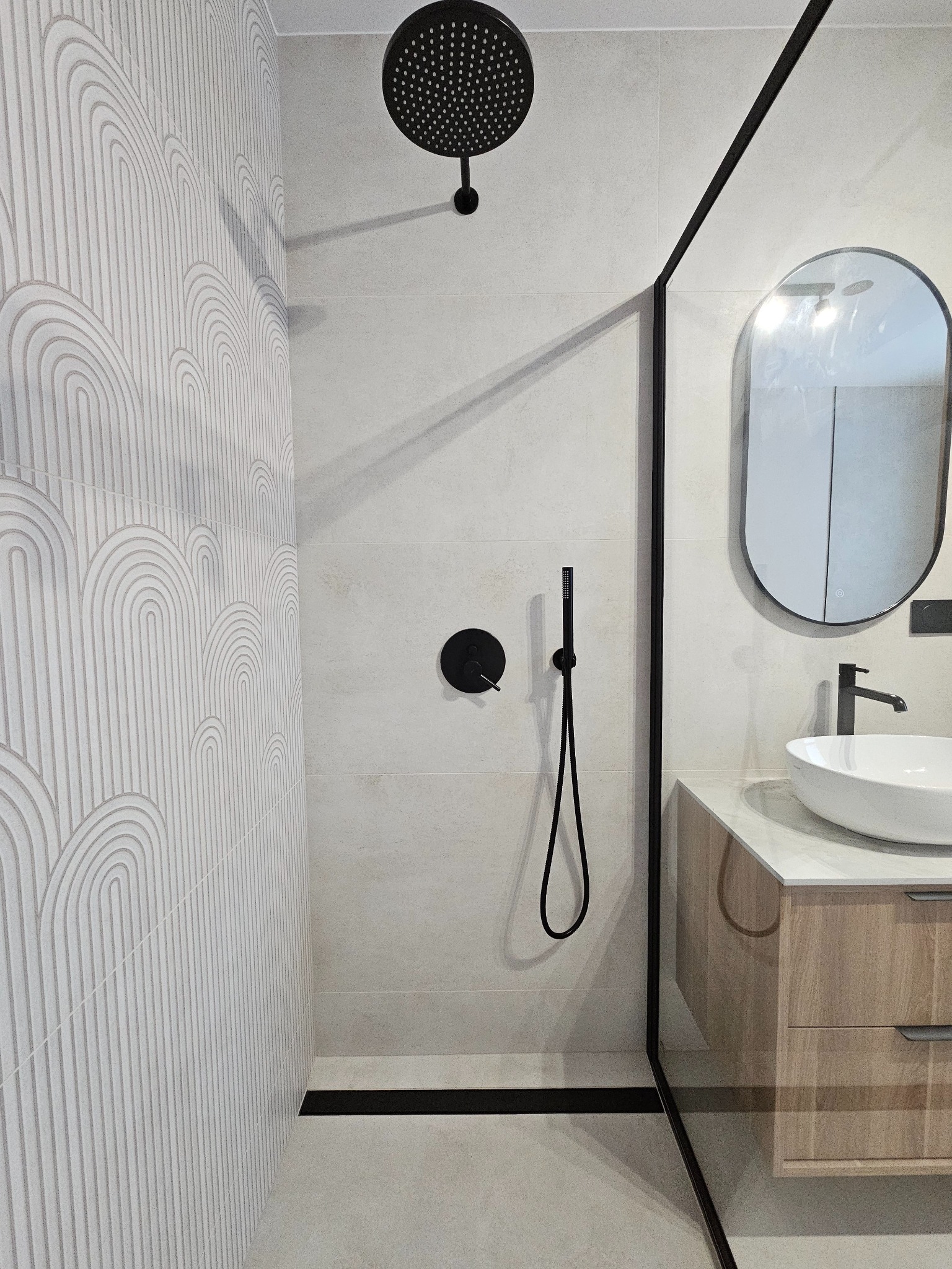 Nowoczesna łazienka z kabiną typu walk-in, białą umywalką nablatową i czarną armaturą. Na ścianie płytki z subtelnym wzorem w łuki.