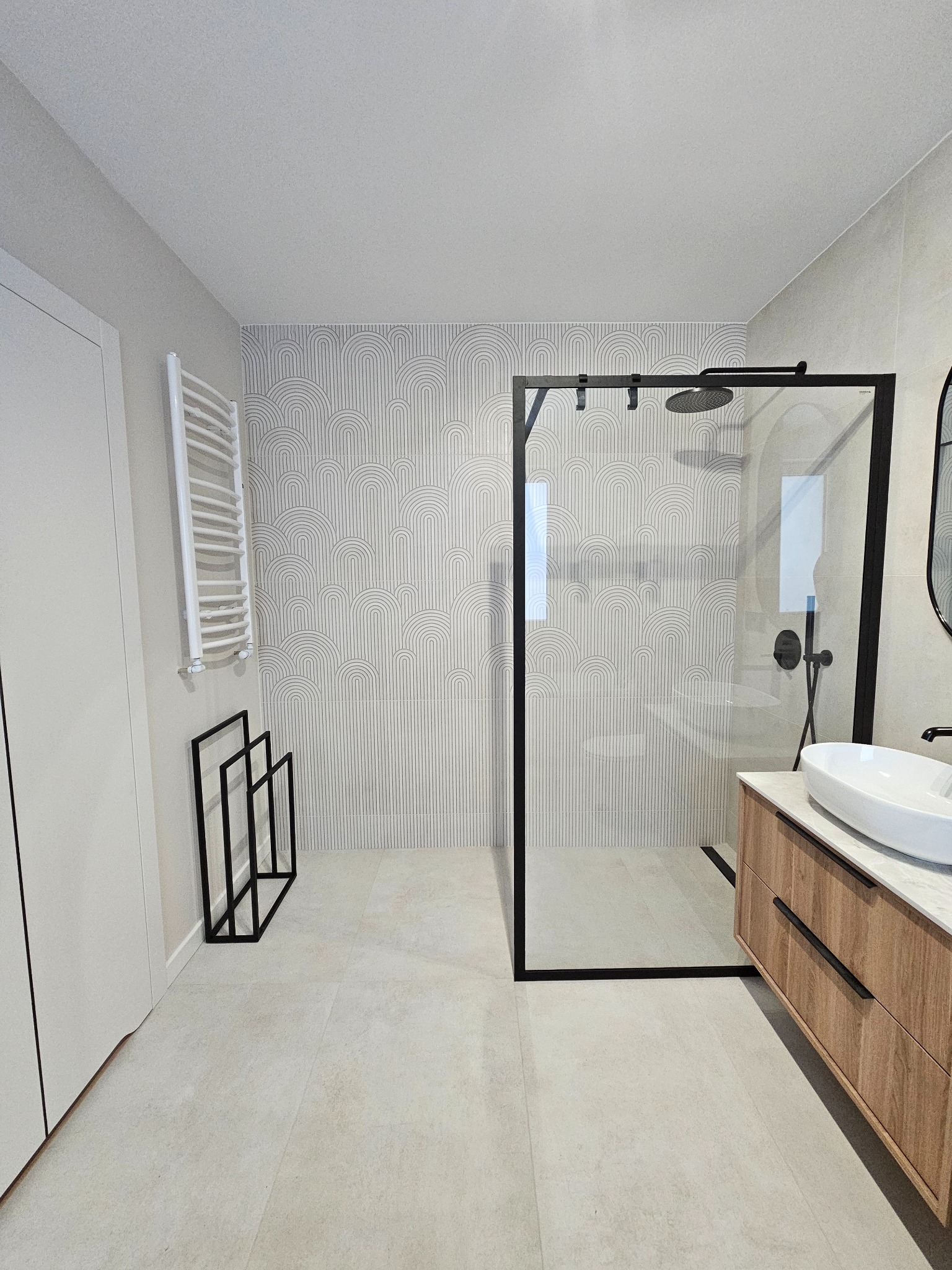 Nowoczesna łazienka z kabiną typu walk-in, umywalką nablatową na drewnianej szafce i grzejnikiem drabinkowym. Ściana z geometrycznym wzorem. Minimalistyczny design.