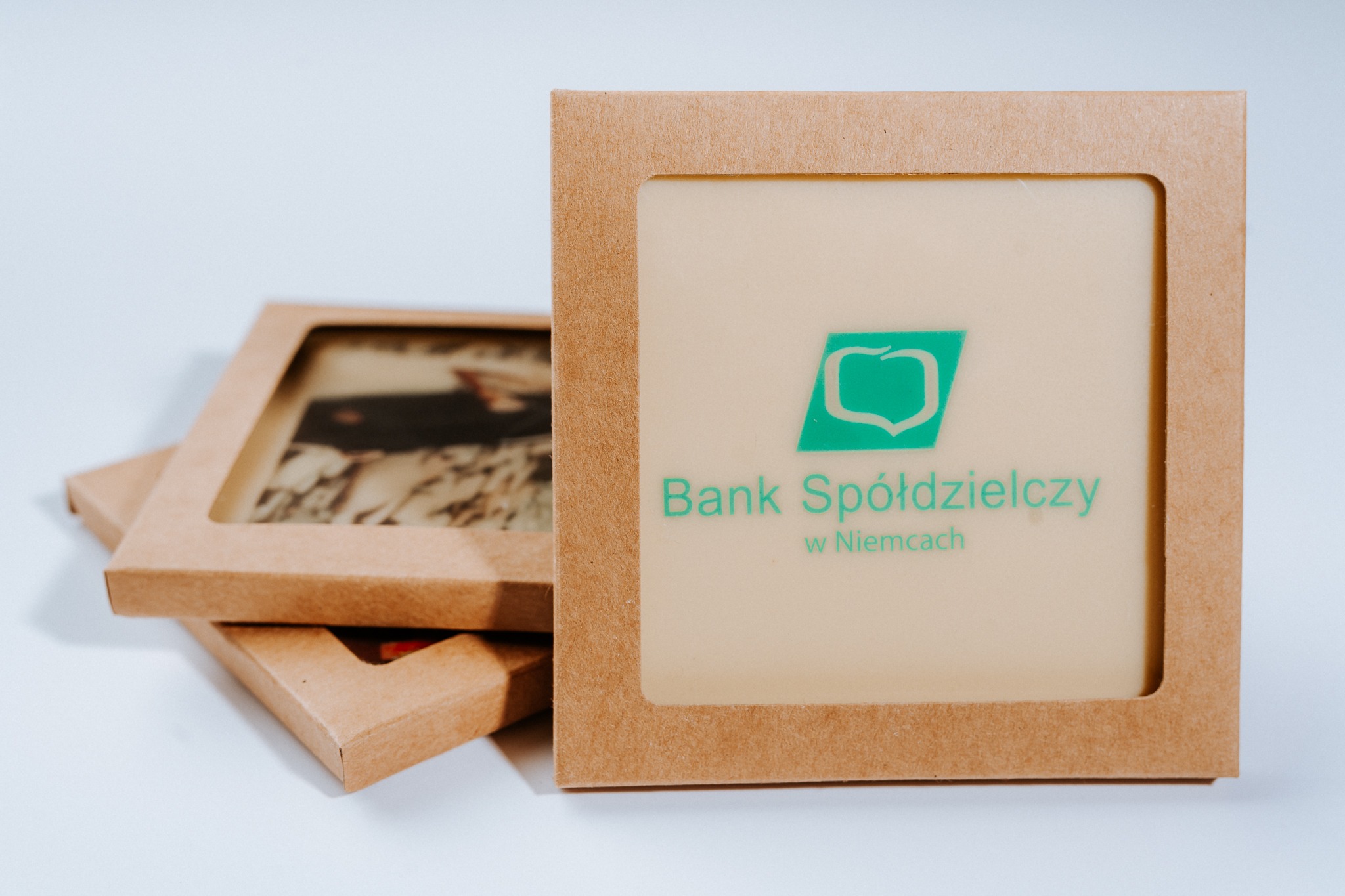 Stos brązowych pudełek z okienkiem, prezentujących logo Banku Spółdzielczego w Niemczach, na białym tle.
