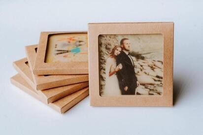 Kosze prezentowe z Lublina zawierające spersonalizowane upominki w ekologicznych, kartonowych opakowaniach z okienkiem, prezentujące zdjęcie ślubne pary i abstrakcyjny rysunek dziecka.