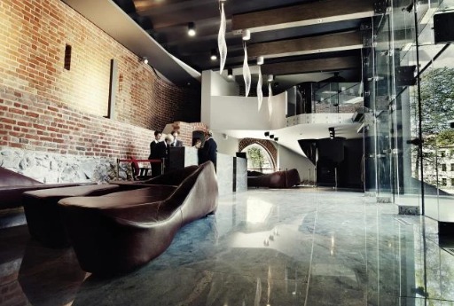 Przestronne lobby budynku usługowego z ceglaną ścianą, marmurową podłogą i nowoczesnymi sofami; recepcja z obsługą w tle.