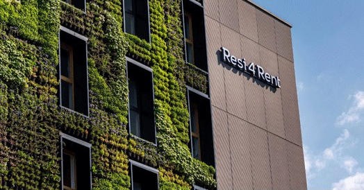 Elewacja budynku usługowego z pionowym ogrodem i logo 'Resi4Rent' na brązowej fasadzie.