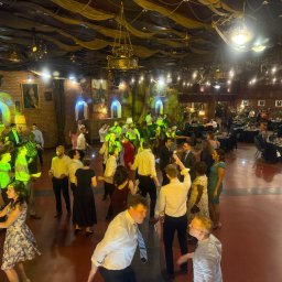 DJ Pawlos Łukasz Pawlos - Sala balowa w stylu zamkowym z tańczącymi gośćmi, oświetlona zielonymi reflektorami i zdobiona żyrandolami. Ustawione stoły z nakryciami w tle.