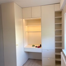 MYCREATOR WALCZAK BARTOSZ - Biała szafa wnękowa z biurkiem i oświetleniem LED, widok z przodu. Na blacie biurka leżą drobne przedmioty. Minimalistyczny design, jasne wnętrze.