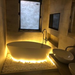 Robert Fritz - Nowoczesna łazienka z wolnostojącą wanną podświetloną od dołu białymi kamieniami, minimalistyczna armatura i telewizor wbudowany w ścianę.