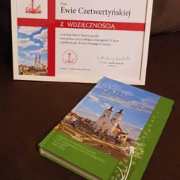 Oprawiona w ramkę dedykacja dla Ewy Czetwertyńskiej z podziękowaniem za wkład w historię parafii i pomoc w publikacji monografii, obok leży książka o 25-leciu parafii rzymskokatolickiej...