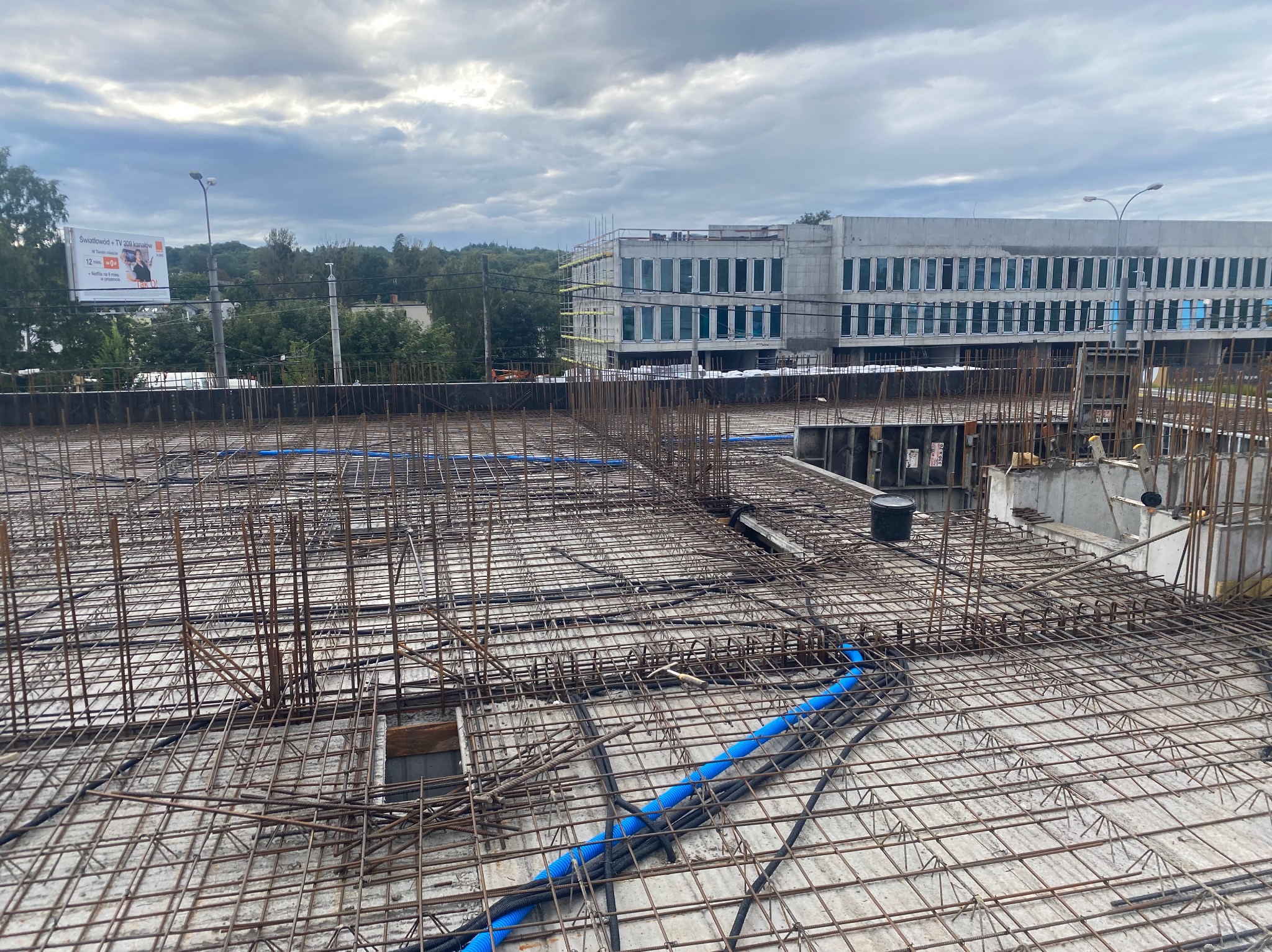 Zbrojenie stropu z widocznymi niebieskimi rurami instalacyjnymi na budowie budynku biurowego w pochmurny dzień. Detal zbrojenia z bliska.
