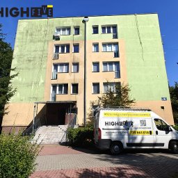 High five usługi alpinistyczne - Wielopiętrowy budynek po częściowym odświeżeniu elewacji, z widocznym firmowym vanem z reklamą usług mycia i malowania dachów i elewacji. Widoczne różnice w kolorze elewacji.