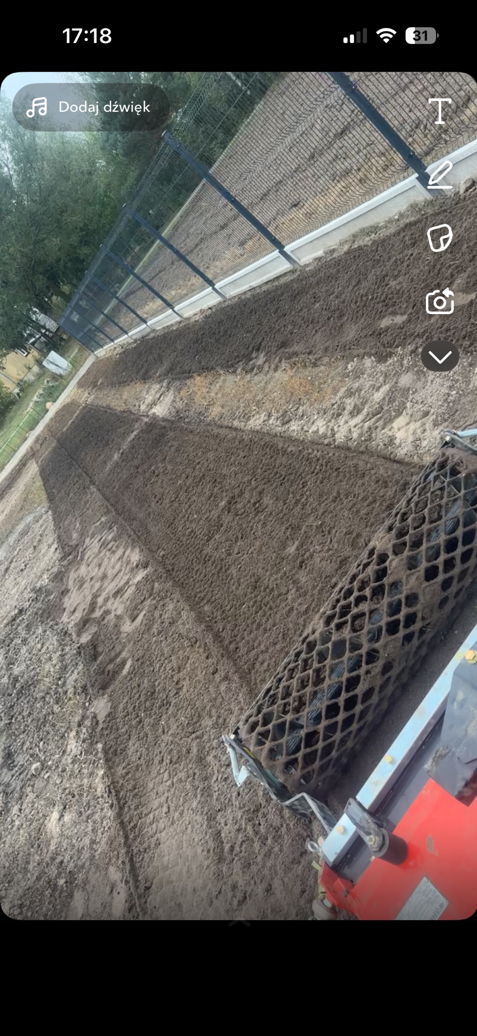 Walec ogrodowy ugniatający świeżo rozłożoną ziemię na przygotowanym terenie pod trawnik, widok z perspektywy operatora maszyny.