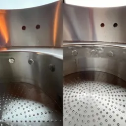 Wnętrze zbiornika ze stali nierdzewnej z perforowanym dnem i otworami na ścianach, widoczne ślady po spawaniu.