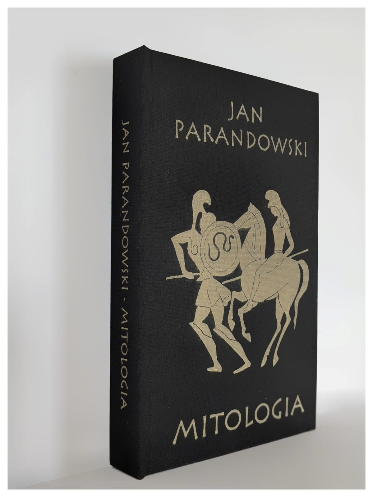 Elegancka, czarna oprawa książki 'Mitologia' Jana Parandowskiego ze złotymi zdobieniami przedstawiającymi postacie mitologiczne. Widoczny bok książki.