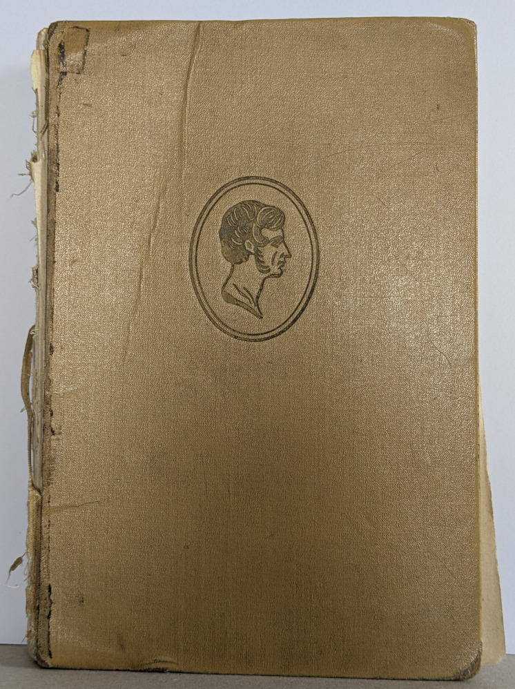 Zniszczona, beżowa oprawa książki z wytłoczonym portretem w owalu. Widoczne uszkodzenia grzbietu i rogów. Introligatorska praca z historią.