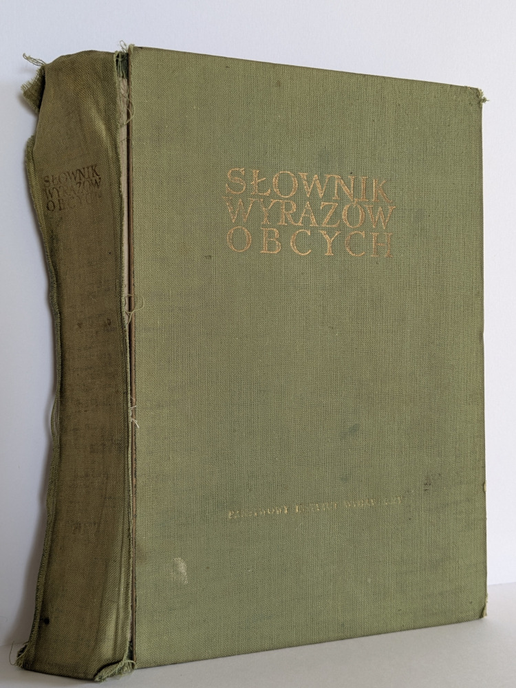 Stary, zielony słownik wyrazów obcych z przetartą okładką i złoconym napisem, ukazujący ślady użytkowania i upływu czasu. Widoczny bok książki.