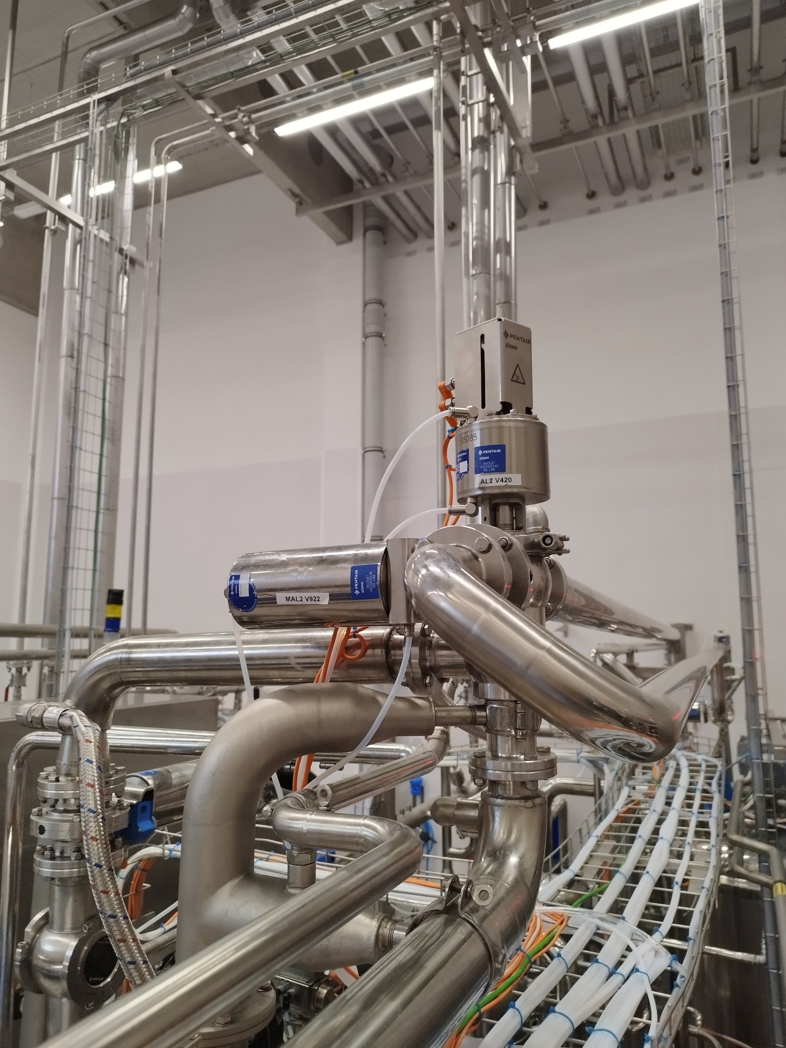 Kompleksowa instalacja przemysłowa z rur ze stali nierdzewnej, widoczne zawory Pentair SUD40 i AL2 V420, oraz okablowanie na metalowej drabince w sterylnym pomieszczeniu.
