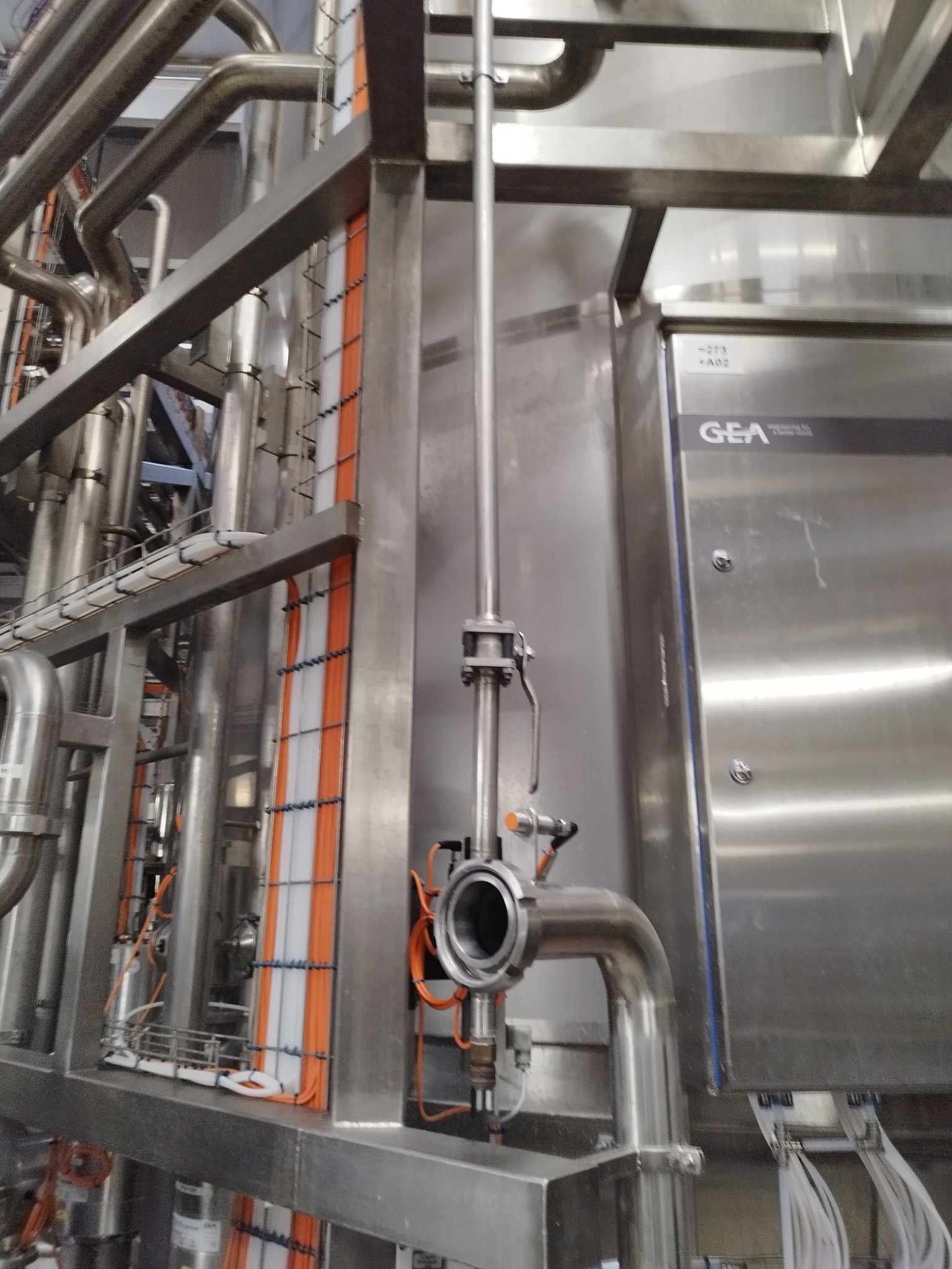 Rozbudowana instalacja przemysłowa ze stali nierdzewnej z licznymi rurami, zaworami i przewodami elektrycznymi, widoczny fragment urządzenia z logo GEA.