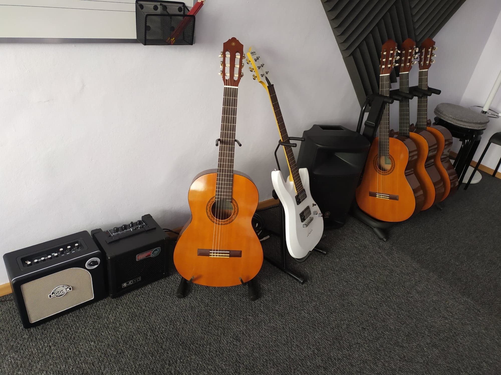 Akustyczne i elektryczne gitary oraz wzmacniacze w pomieszczeniu z panelami akustycznymi na ścianie.
