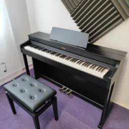 Czarne pianino cyfrowe Casio z ławą na fioletowym dywanie, panele akustyczne na ścianie