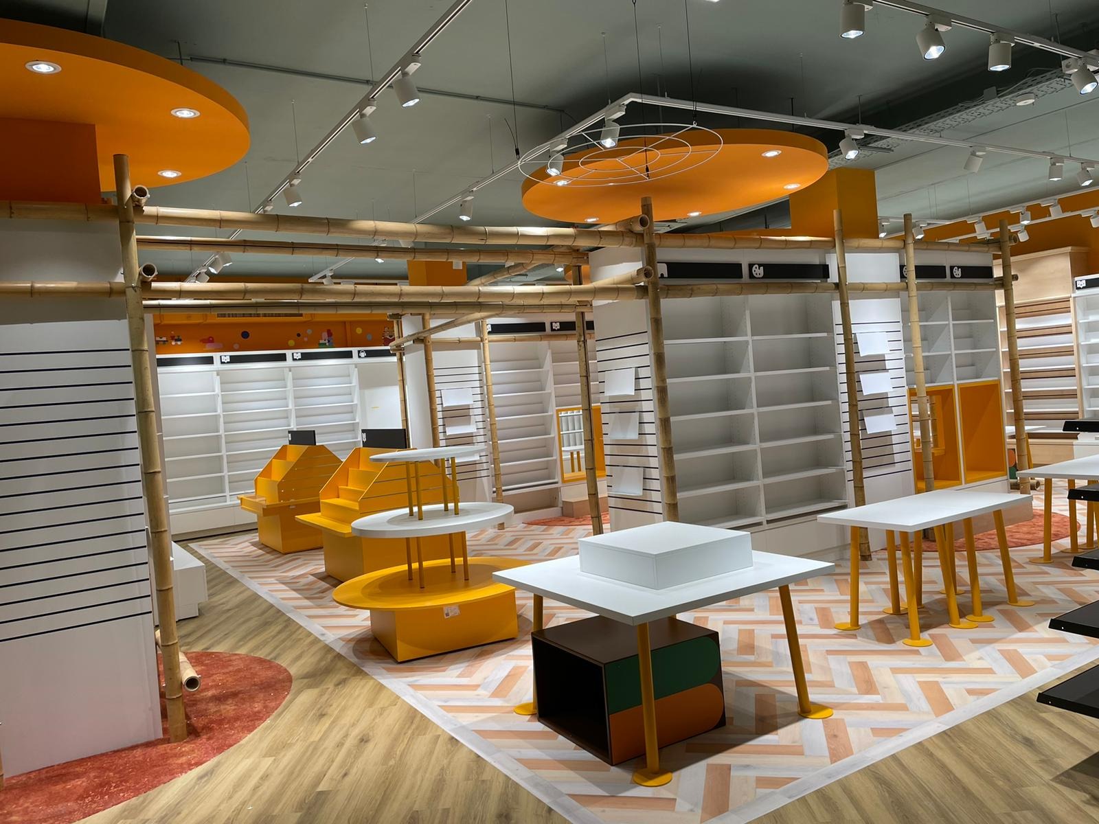 Wnętrze nowo urządzonego sklepu z bambusowymi elementami konstrukcyjnymi, pomarańczowymi akcentami kolorystycznymi na suficie i podłodze, białymi regałami i ekspozytorami oraz wzorzystą podłogą.