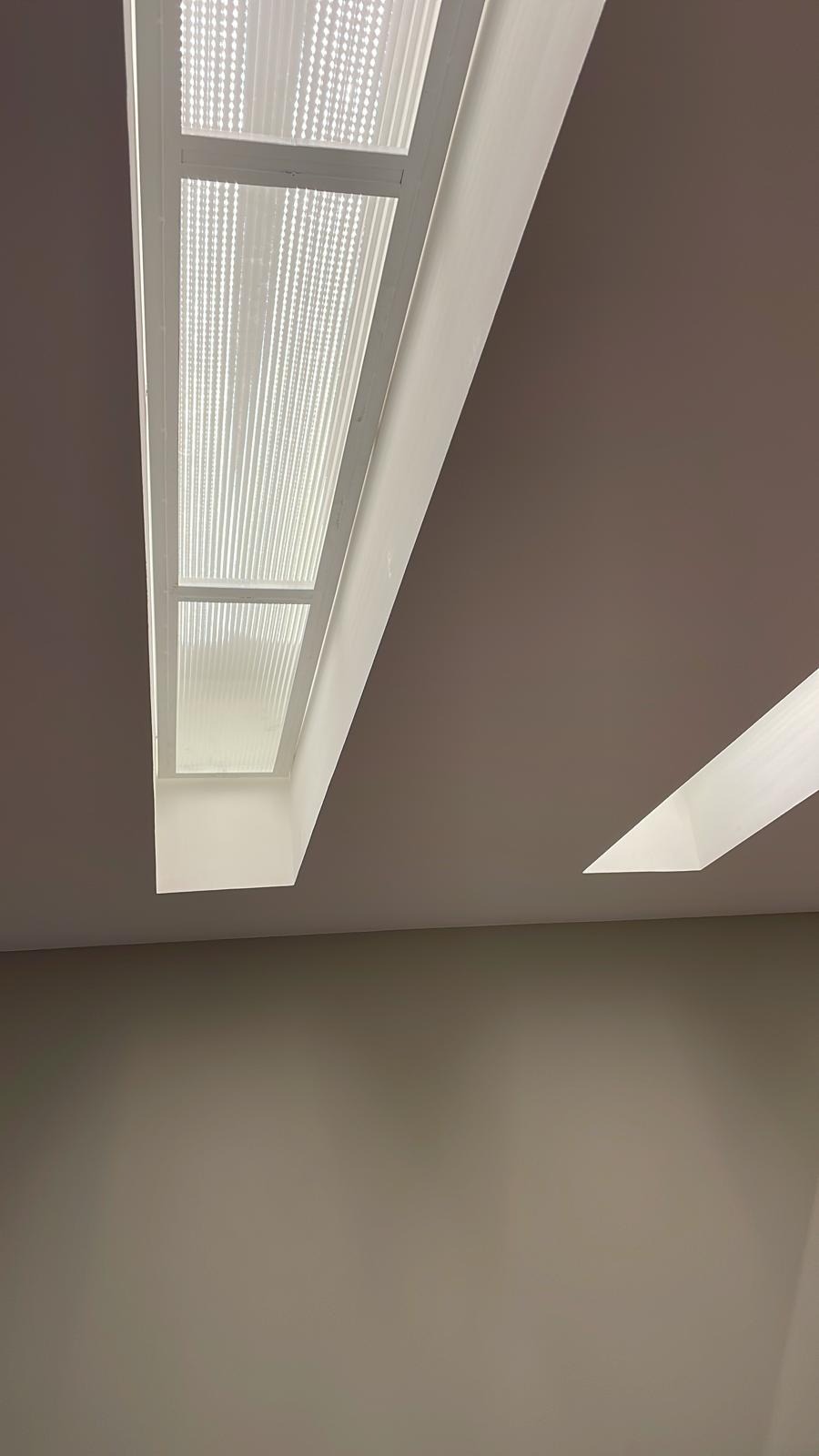Widok na sufit z dwoma wbudowanymi lampami: jedną dużą prostokątną z żebrowanym dyfuzorem i drugą mniejszą, również prostokątną z gładkim dyfuzorem, na tle beżowej ściany.