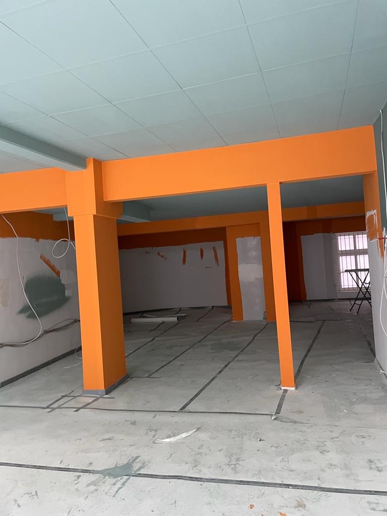 Wnętrze w trakcie prac wykończeniowych: pomarańczowe filary i belki na tle surowych ścian, zabezpieczona podłoga, sufit z kasetonów.