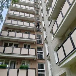 Pracownik w kasku, na linie, w trakcie pracy na wysokości na elewacji wysokiego budynku z balkonami.