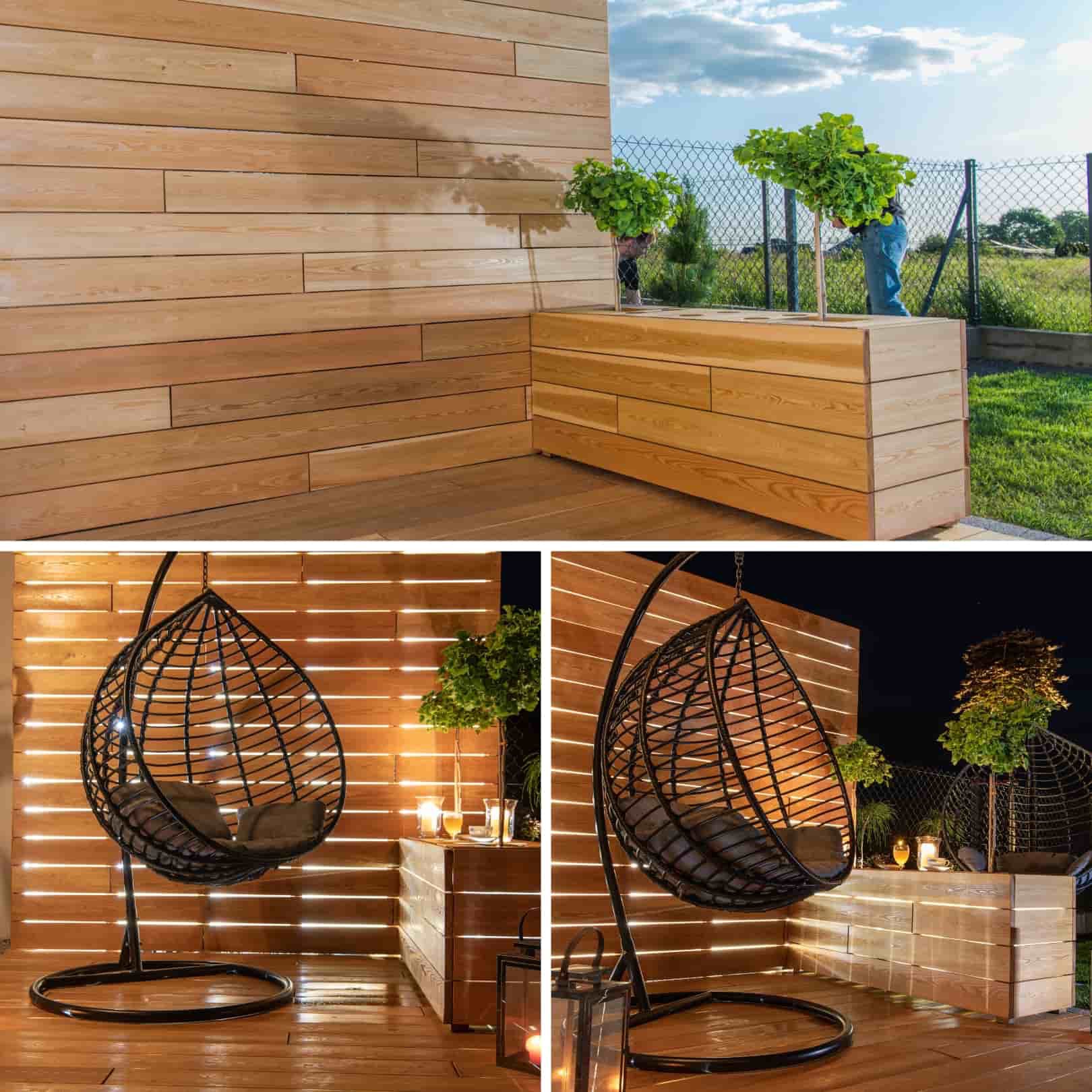Drewniany taras z wiszącymi fotelami typu kokon, oświetlony lampionami i świecami, z drewnianą ścianą i donicami z drzewkami kulistymi, w tle widok na ogród.