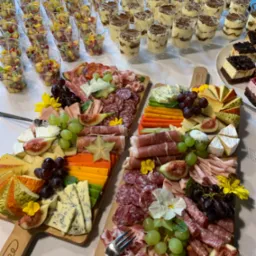 Bogato zastawiony st&oacute;ł z deskami ser&oacute;w i wędlin, deserami w szklankach i ciastami, idealny na przyjęcie.