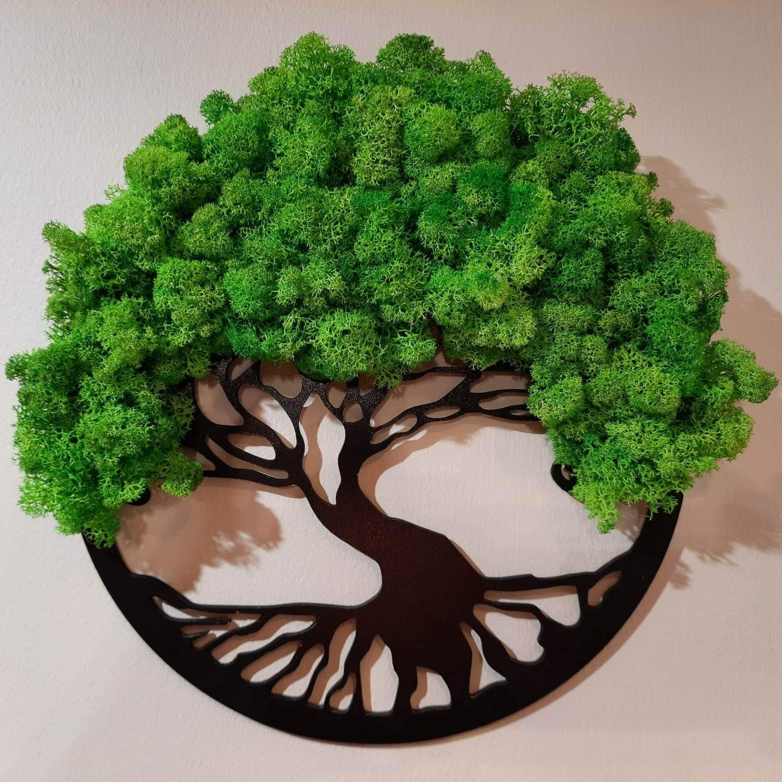 Dekoracja ścienna: metalowa sylwetka drzewa z koroną z mchu stabilizowanego, umieszczona na białej ścianie.