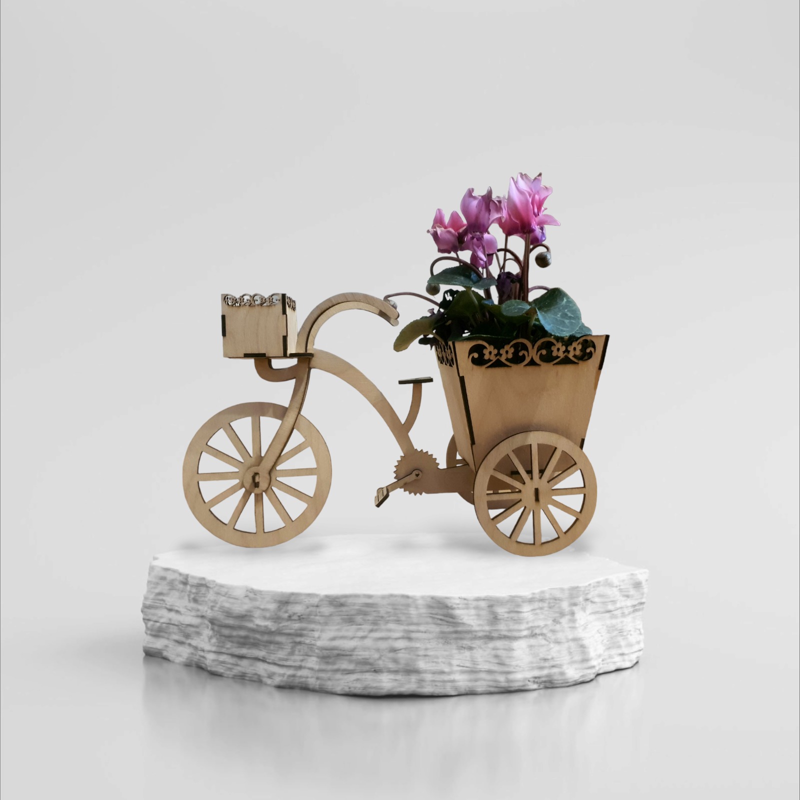 Ozdobny drewniany trójkołowy kwietnik z cyklamenami, umieszczony na białym postumencie.