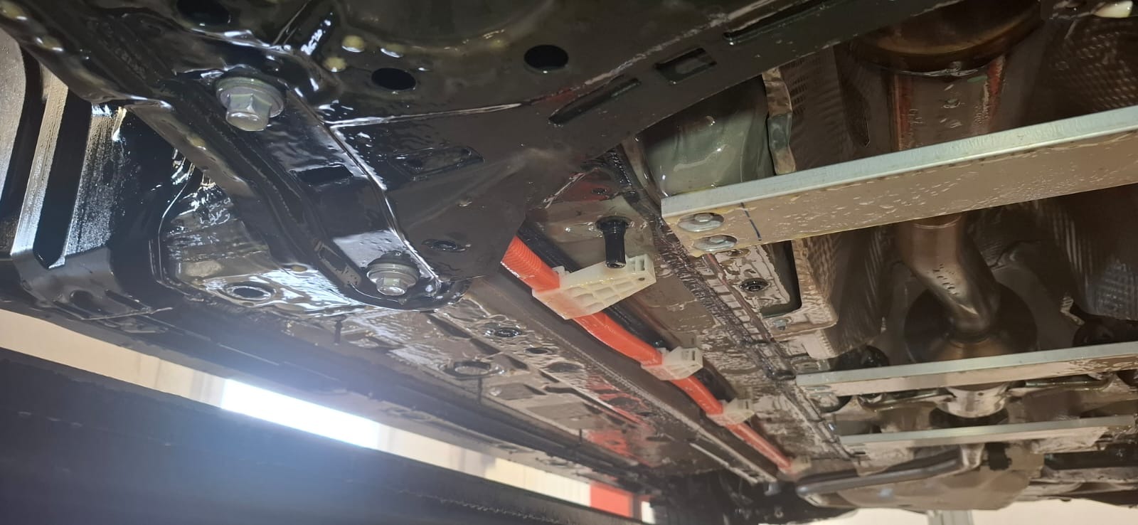 Podwozie samochodu po konserwacji antykorozyjnej, widoczne elementy zawieszenia, przewody w pomarańczowej osłonie i świeża warstwa ochronna.