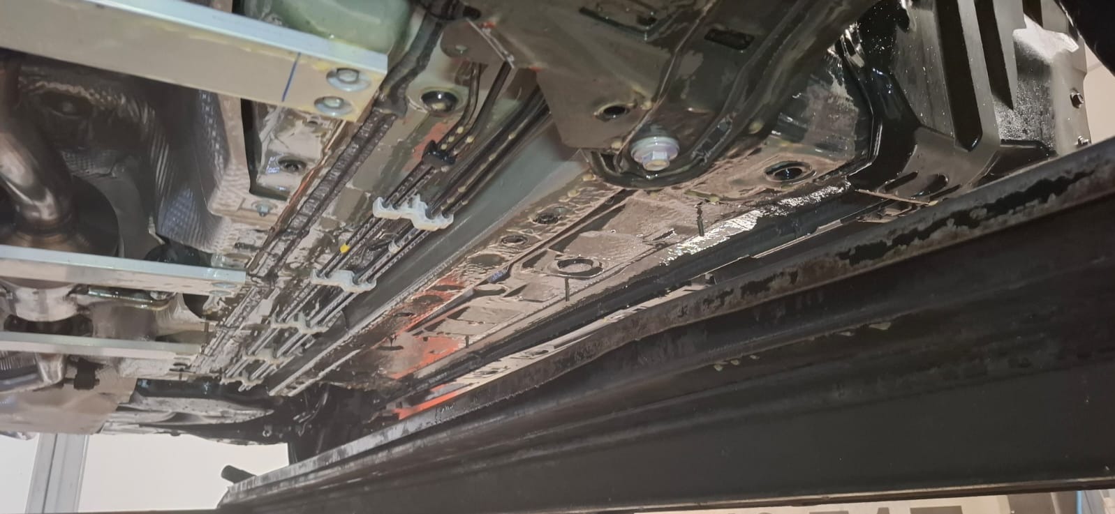 Spód auta po konserwacji antykorozyjnej, widoczny na podnośniku warsztatowym. Detale zabezpieczonej ramy, przewodów i elementów zawieszenia.