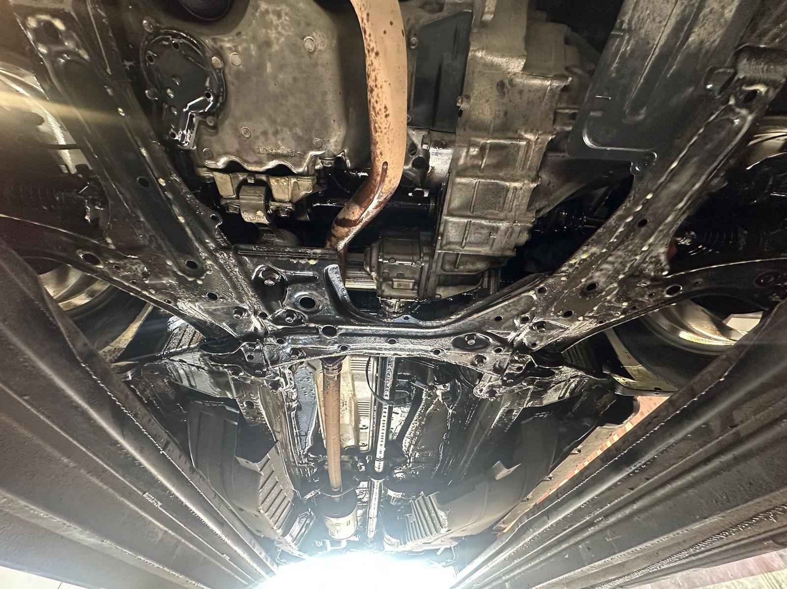 Podwozie auta po zabezpieczeniu antykorozyjnym, widok od spodu. Elementy metalowe pokryte czarną, błyszczącą powłoką ochronną. Widoczne detale konstrukcyjne pojazdu.