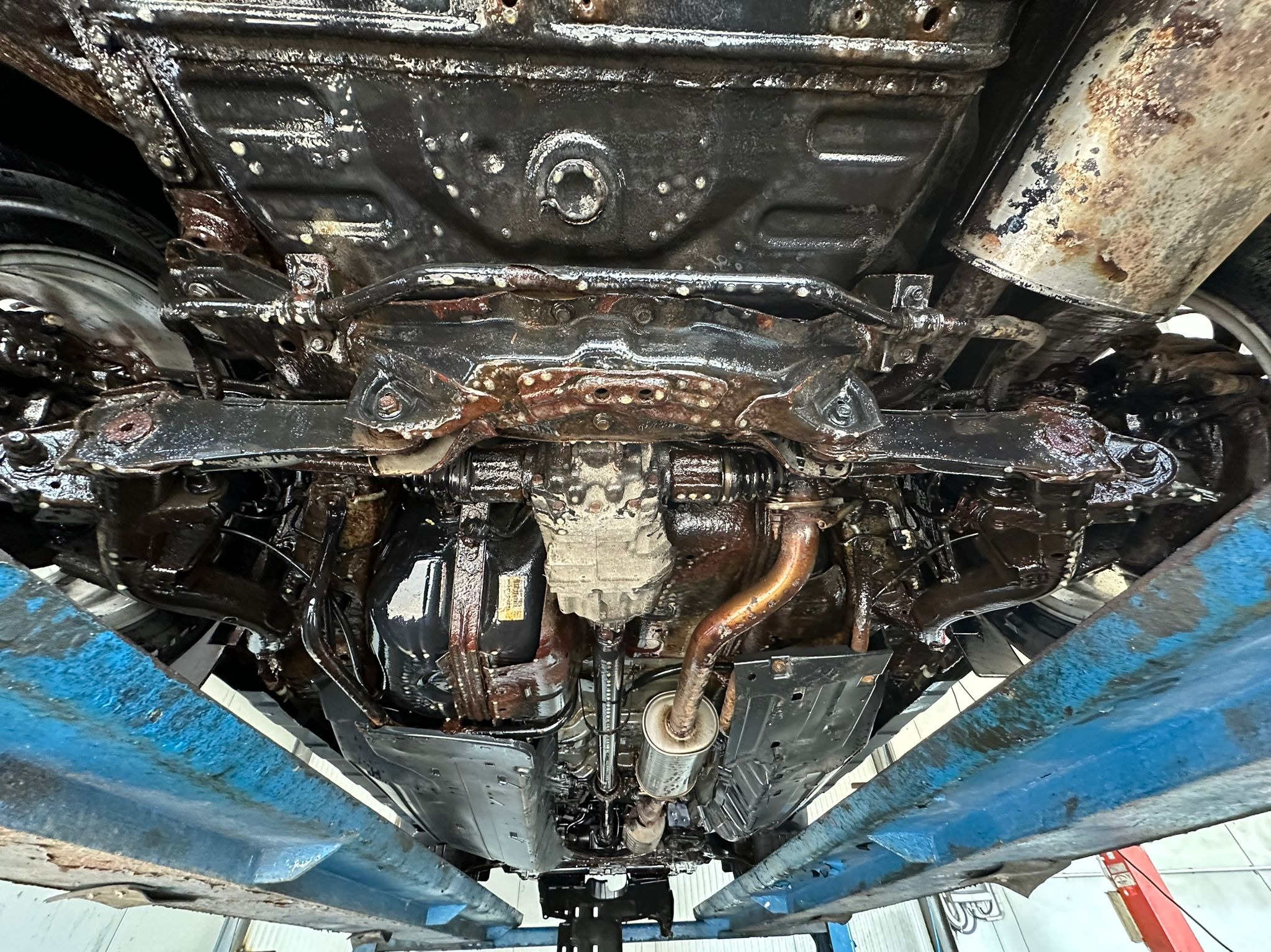 Podwozie samochodu po konserwacji antykorozyjnej, widoczne elementy zawieszenia i układu wydechowego pokryte ochronną warstwą na podnośniku warsztatowym.