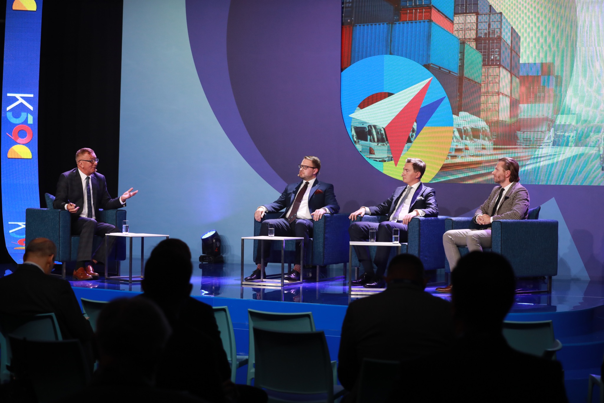 Adwokat Radosław Płonka przemawia podczas debaty na Kongresie 590, siedząc w fotelu obok innych prelegentów na scenie z abstrakcyjnym tłem przedstawiającym kontenery transportowe i logo wydarzenia.