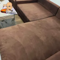 Brązowa, modułowa kanapa z widocznymi śladami czyszczenia, z logo firmy naklejonym na stole w tle.