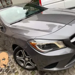 Błyszczący, szary Mercedes CLA po umyciu, zaparkowany na brukowanym podjeździe, z widocznym logo firmy detailingowej w lewym dolnym rogu.